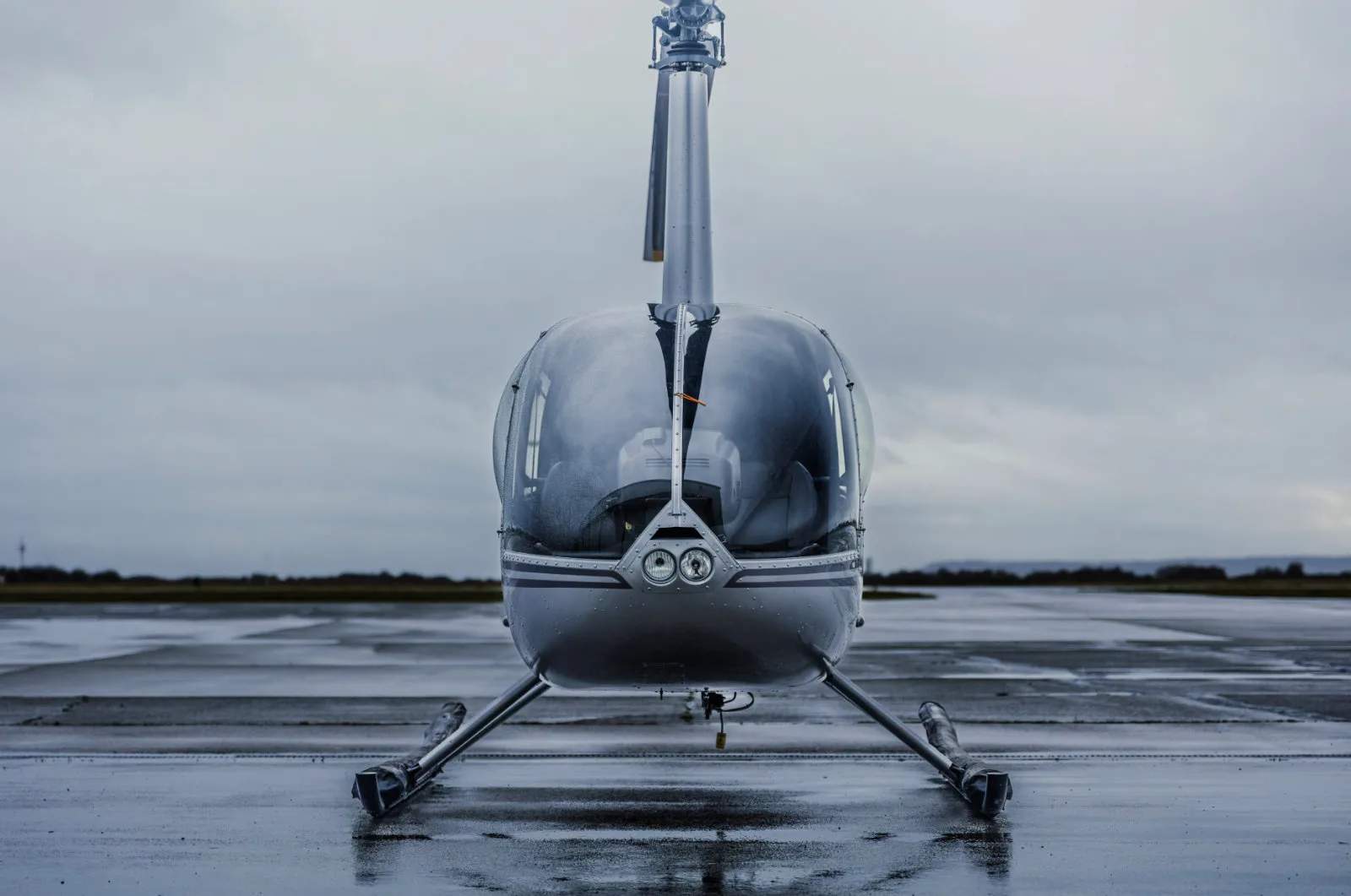Front view of a Robinson helicopter on a wet tarmac.