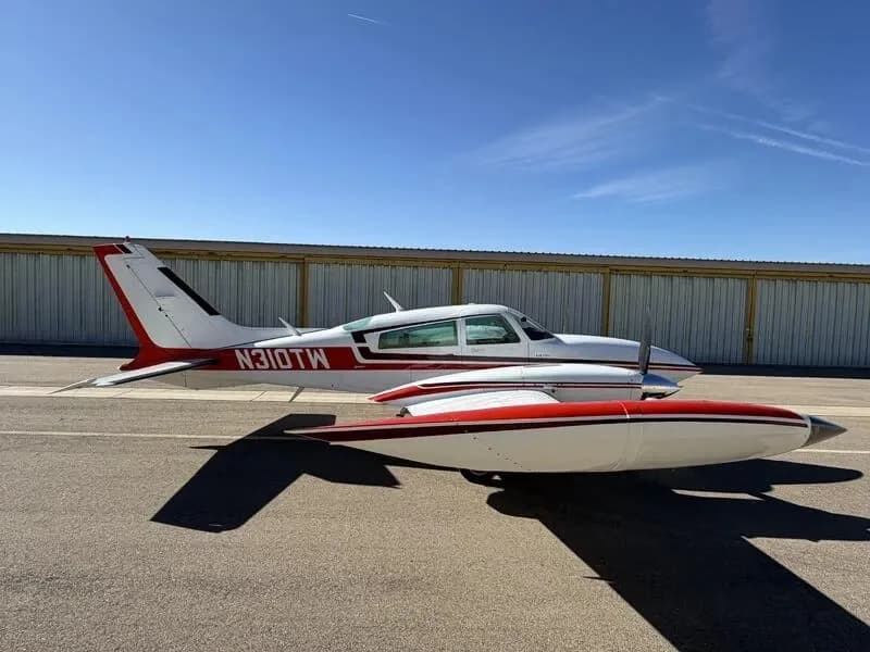 Side view of a white and red Cessna 310 twin-engine aircraft with tip tanks parked on an airfield.