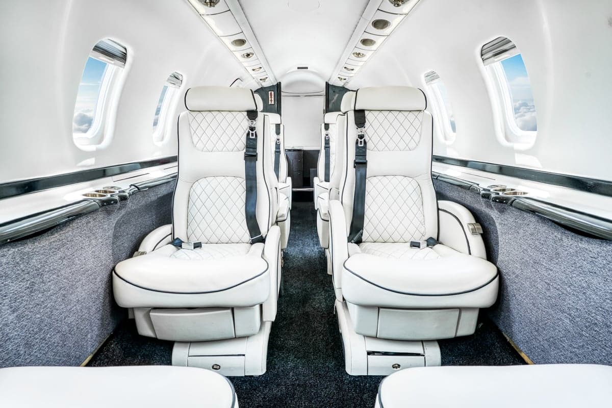 The elegant white leather interior of a private jet cabin featuring quilted seats and windows revealing clouds.