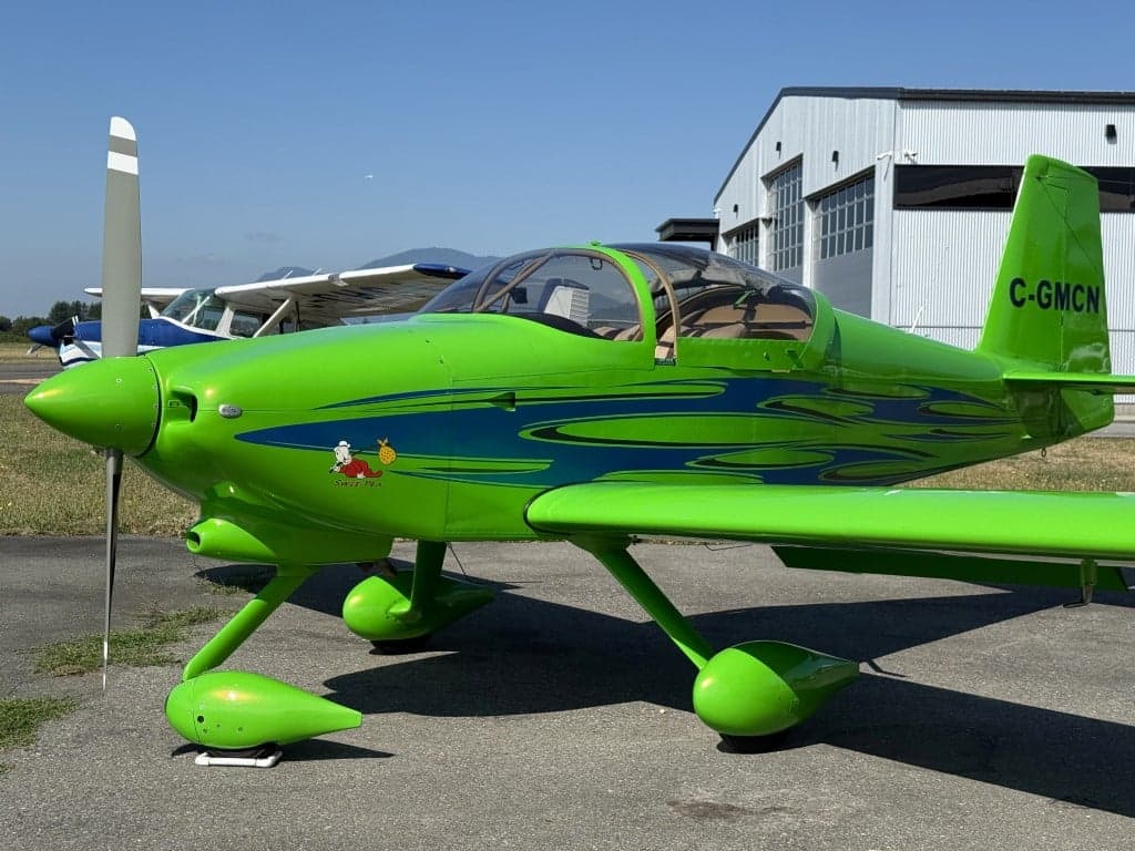 A green aircraft with blue accents parked on the tarmac in front of a hangar.