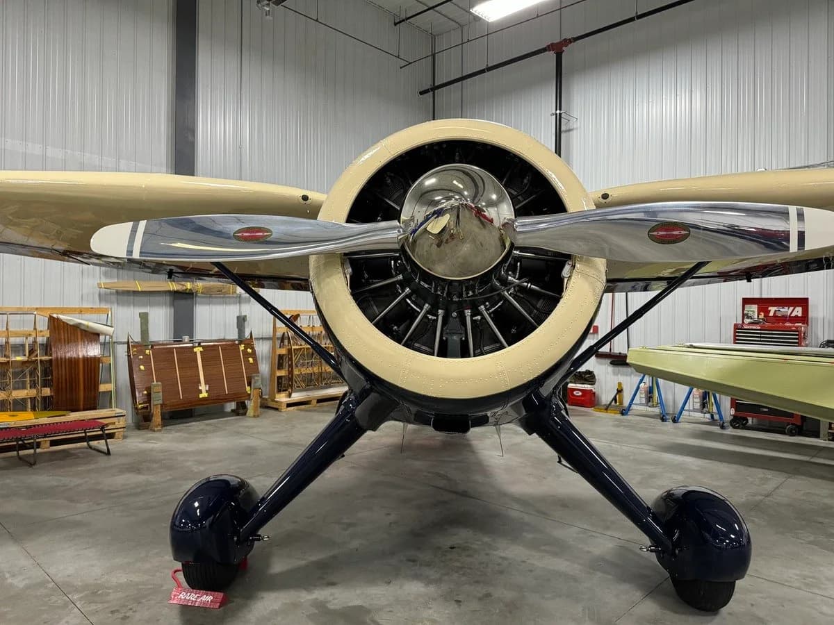 A head-on view of a dark blue and cream vintage aircraft in a hangar, highlighting its polished propeller and engine cowling.