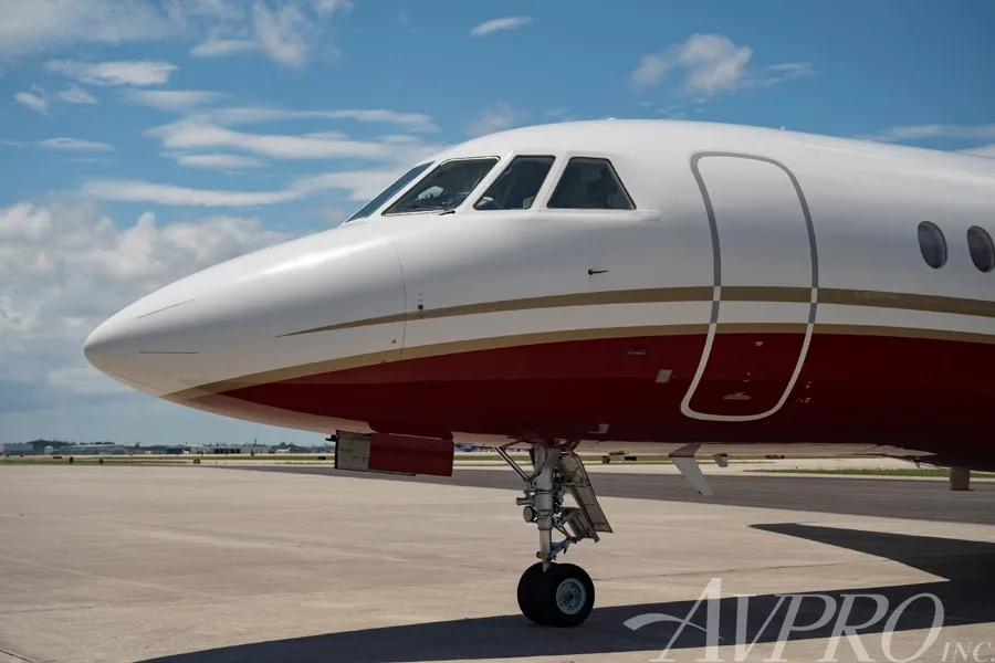 Close-up view of the nose and front landing gear of the Dassault Falcon 900LX, showing its white and red paint scheme.