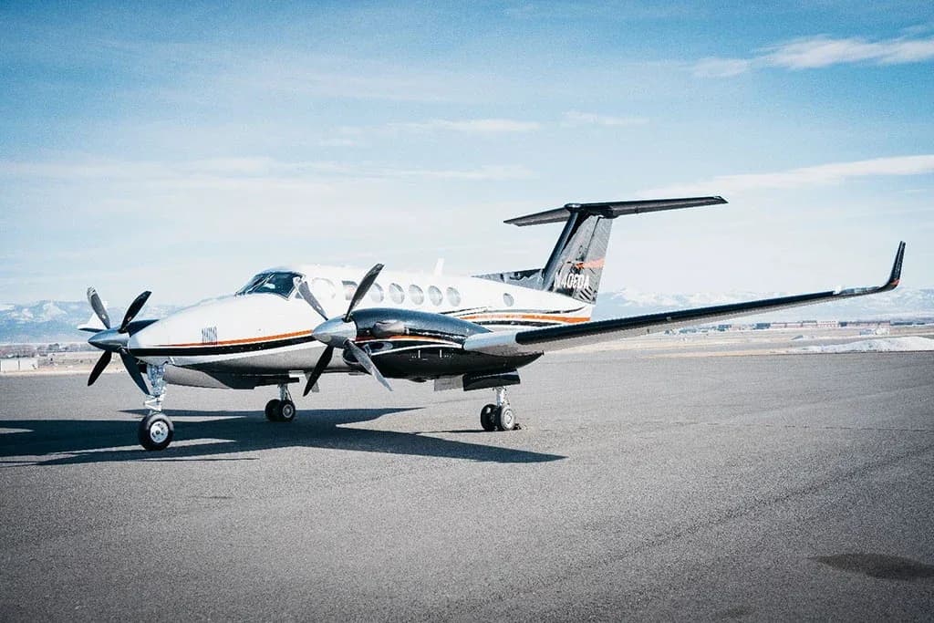 A white and black twin-turboprop aircraft, tail number N405DA, parked on an airfield with mountains in the background.