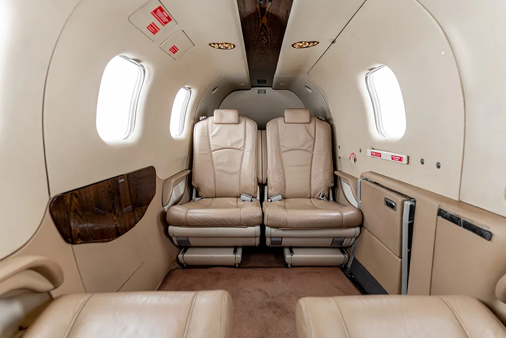 A view of the aircraft cabin with two rows of light beige leather seats and windows.