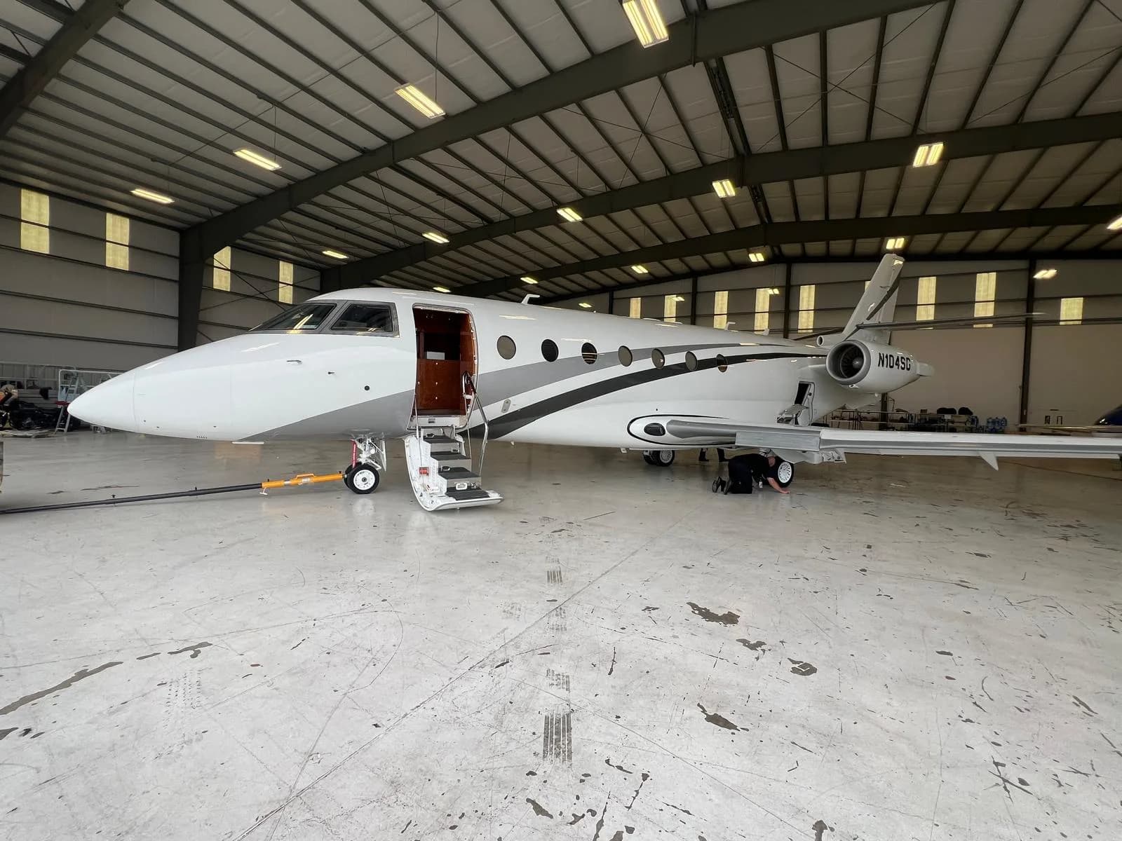 A white and gray jet with tail number N104SG sits inside a hangar with the door open.