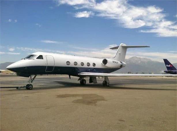 A Gulfstream G-IV business jet, registration N234LR, in a white and dark blue paint scheme, parked on an airport tarmac with mountains in the background.