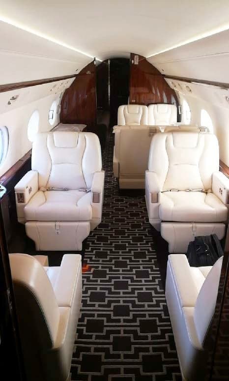 Aisle view of the aircraft cabin with cream-colored leather seats and a patterned carpet.