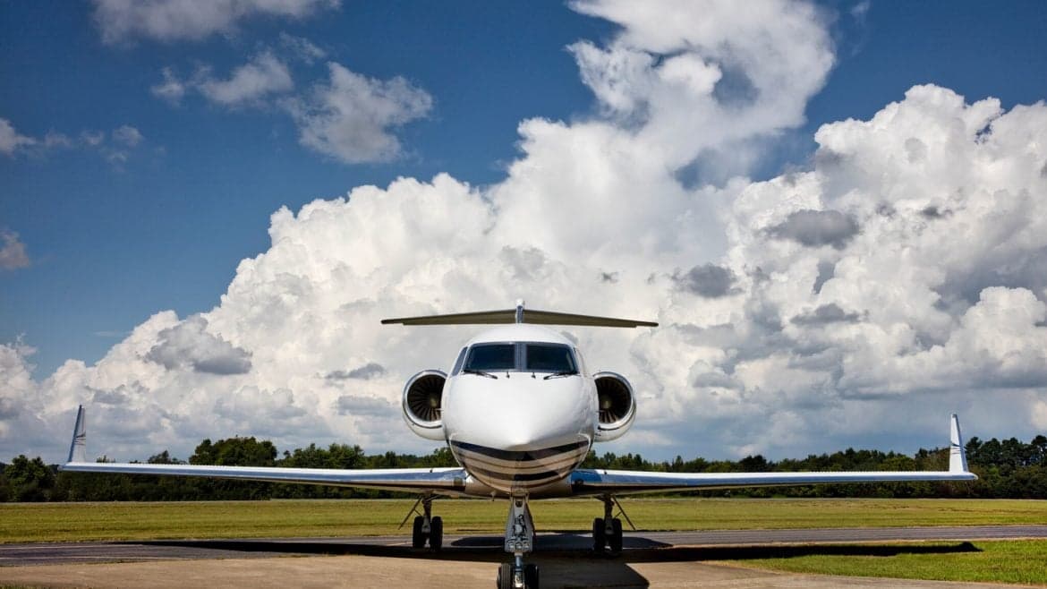 Front view of a white jet aircraft on the tarmac with a cloudy sky background.