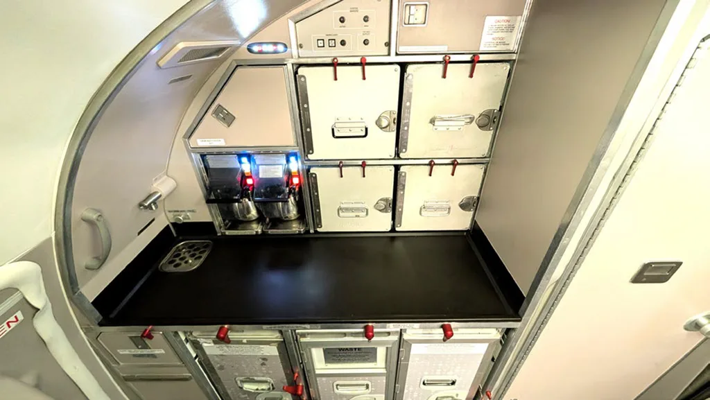 An aircraft galley area with coffee machines and stacked storage compartments.