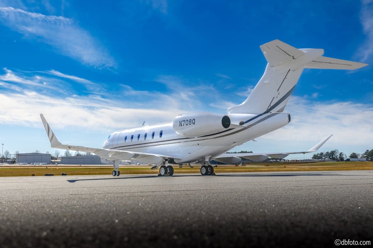 A rear-quarter view of the white Bombardier Challenger N708Q business jet on an airport tarmac.
