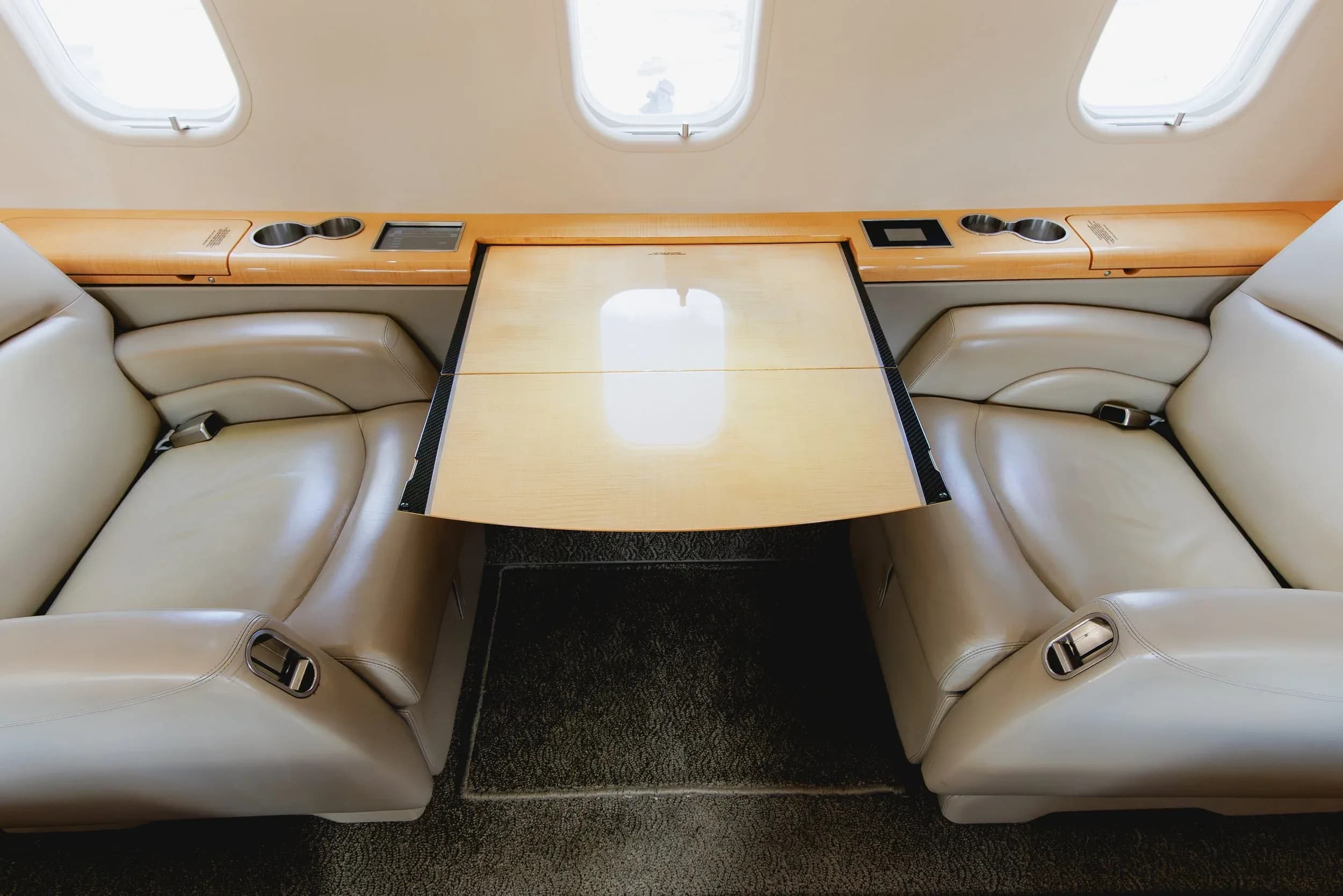 A light wood table extended between two light beige leather seats in a private jet cabin.