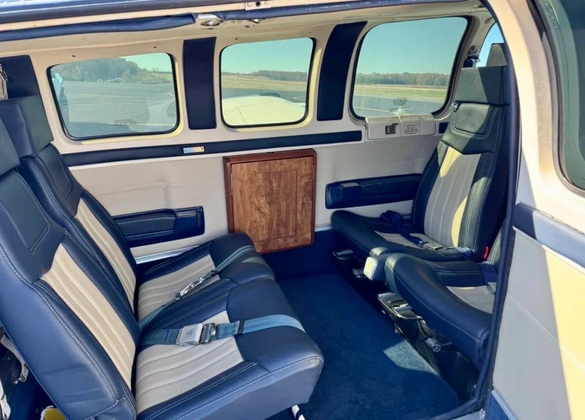 The interior of the aircraft features blue and beige leather seats and a wooden cabinet.