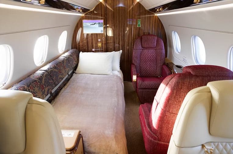 A view of the interior of the aircraft with cream-colored leather seats and a wooden table.