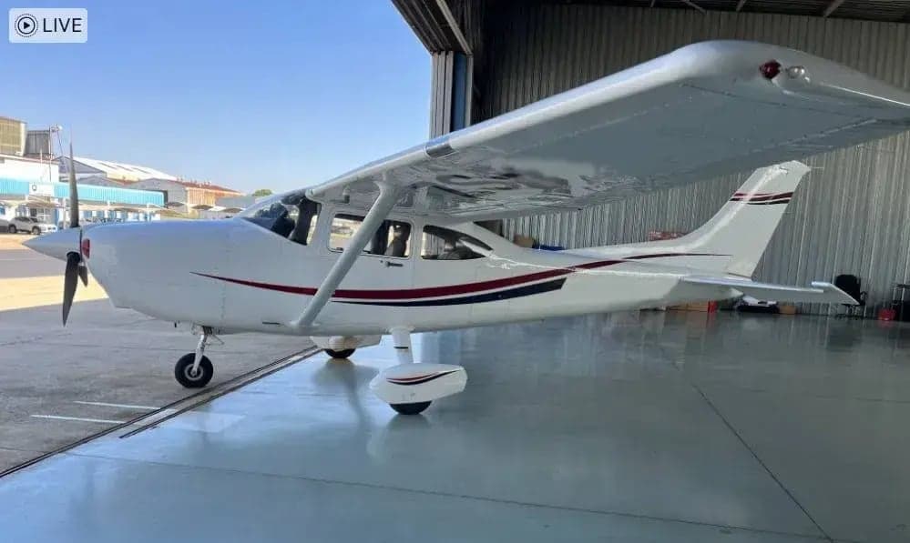 A Cessna aircraft is parked inside a hangar, showcasing its white paint scheme with red and blue accents.