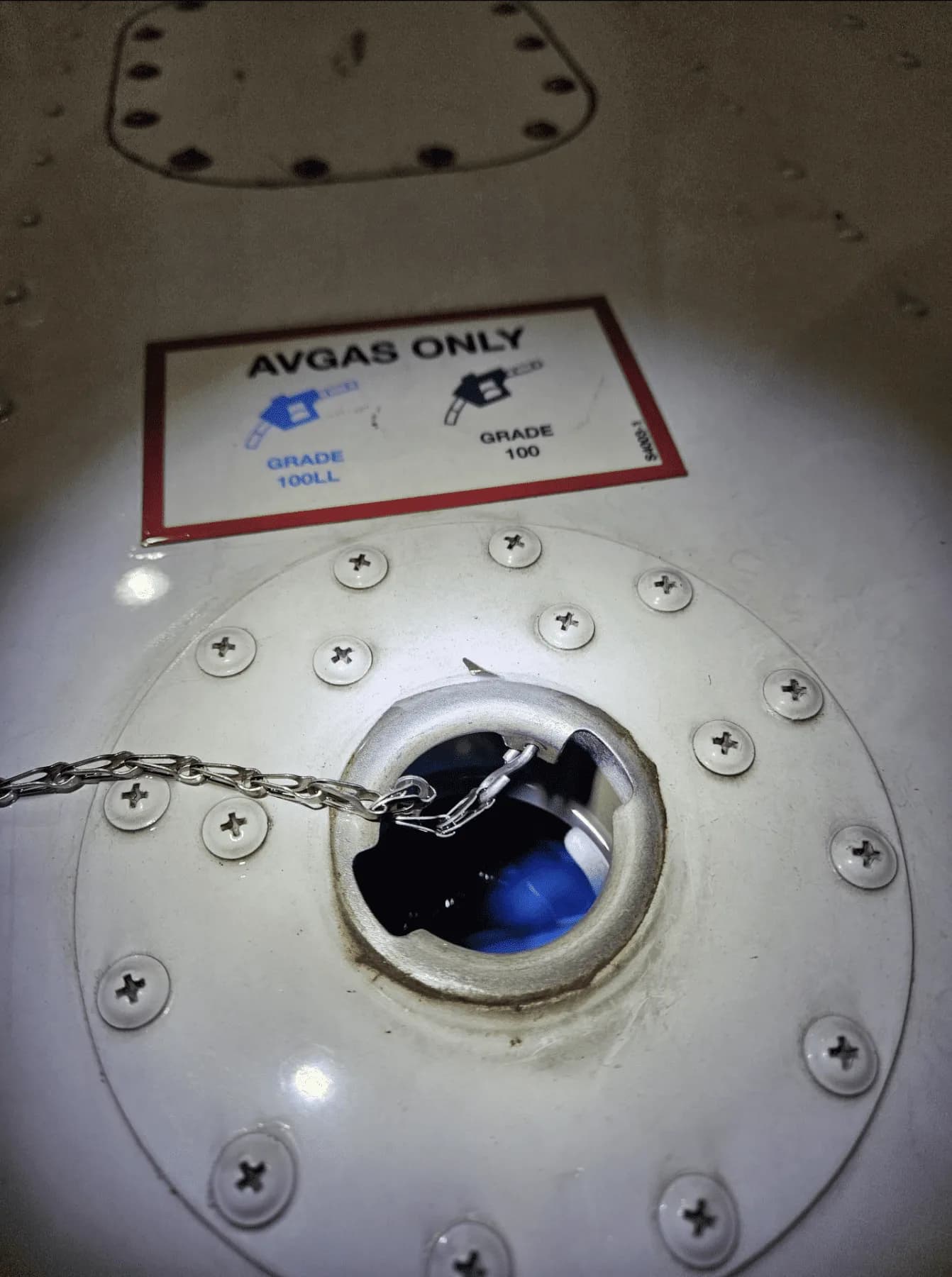 A close-up of an aircraft fuel filler cap with an "AVGAS ONLY" label indicating 100LL and 100 grades.