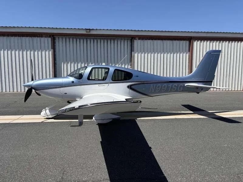 A side view of a blue and white Cirrus SR22 aircraft, registration N991SG, parked on an airfield.