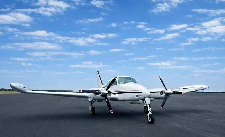 A white twin-engine propeller aircraft with black and gold stripes on an asphalt runway under a blue sky.