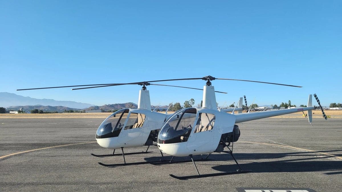 A slightly different angle of two white Robinson R22 helicopters parked on an airport tarmac.