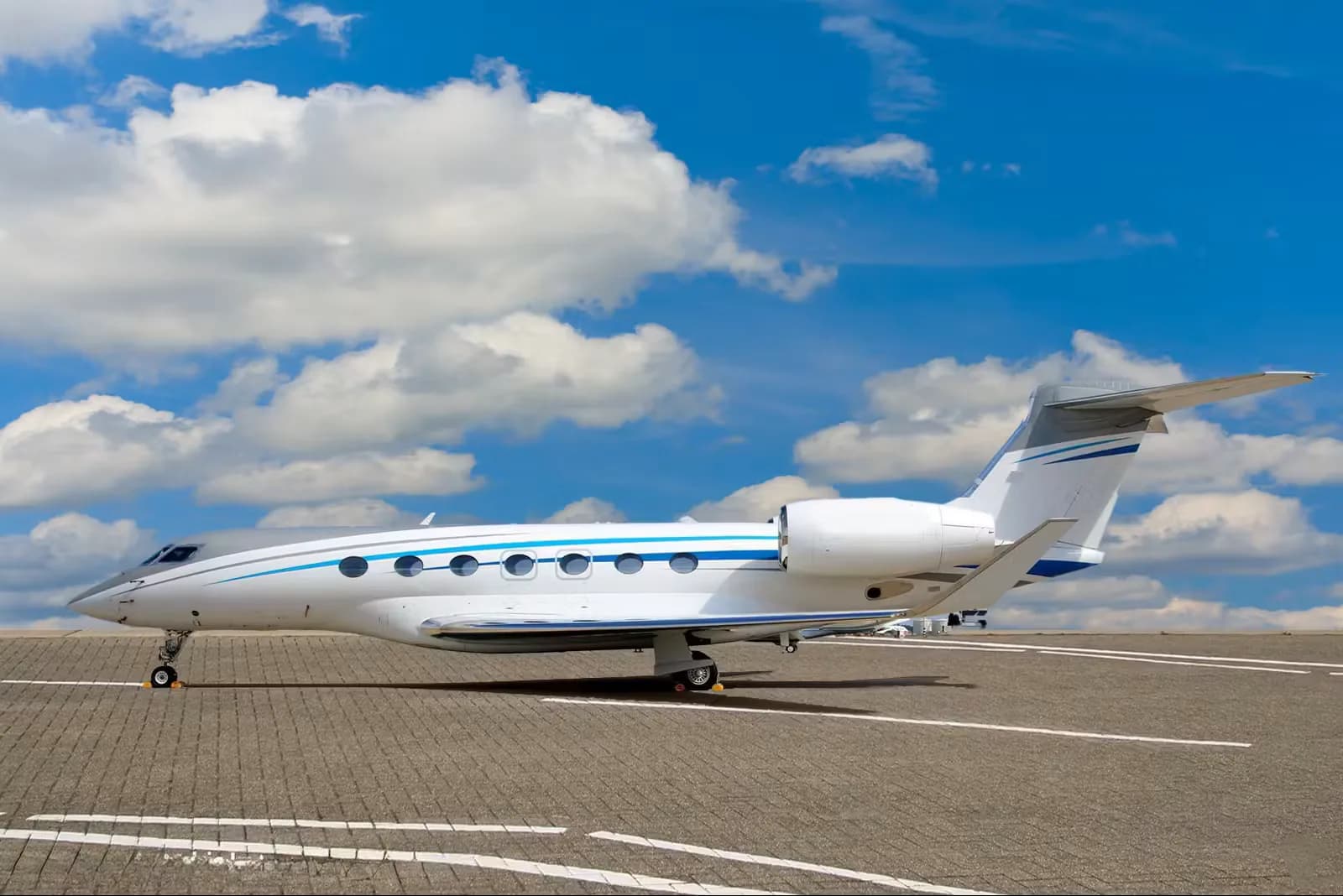 A white and silver Gulfstream business jet is parked on the tarmac under a blue sky with puffy clouds.