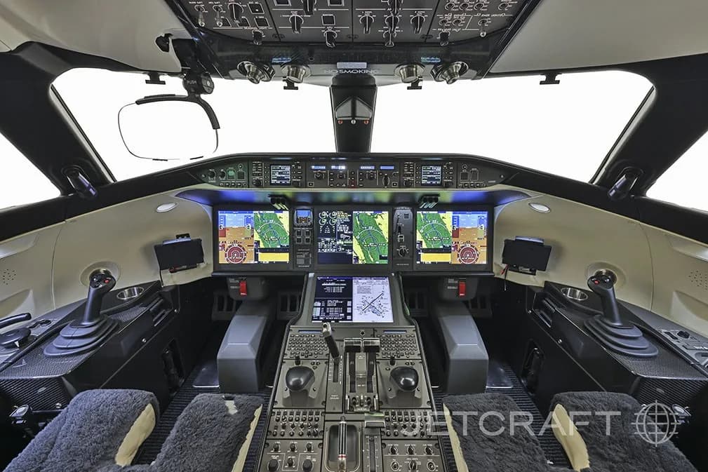 The cockpit of a modern business jet with multiple digital displays and side-stick controls.