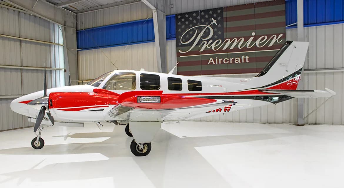 A side view of a white and red twin-engine propeller aircraft, a Beechcraft Baron, in a hangar.