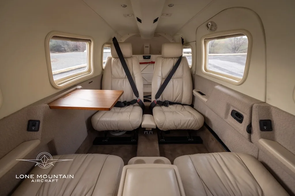 The beige leather interior cabin of the aircraft, showing two rear-facing seats with a table and two forward-facing seats.