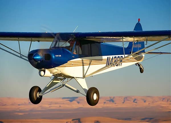 A blue and white Top Cub aircraft in flight over a desert landscape.