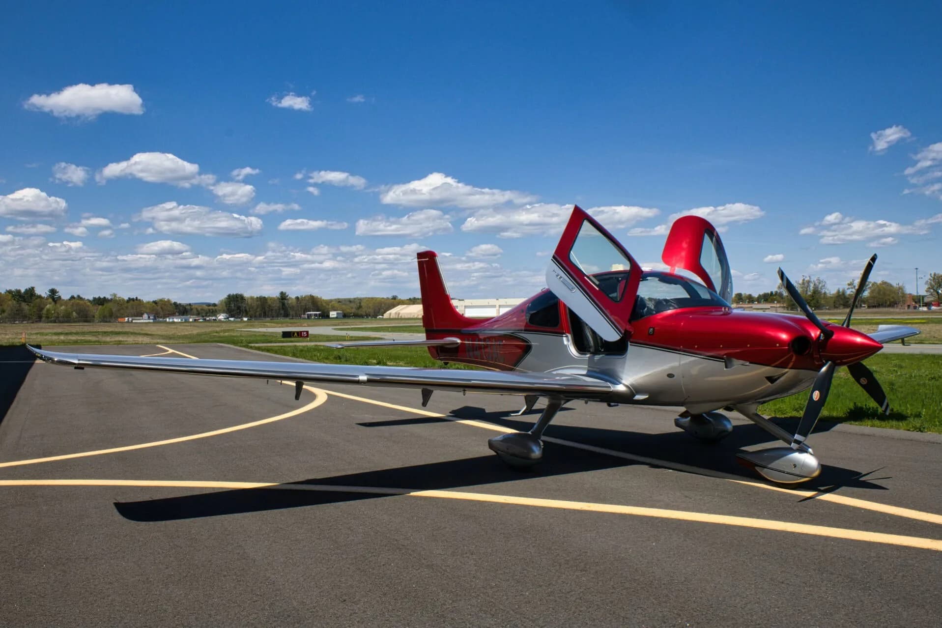 A red and silver Cirrus SR22T aircraft, N413AC, with its gull-wing doors open, parked on an airport tarmac.