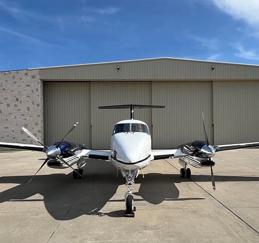 Front view of King Air aircraft N711VN parked on the tarmac in front of a hangar.