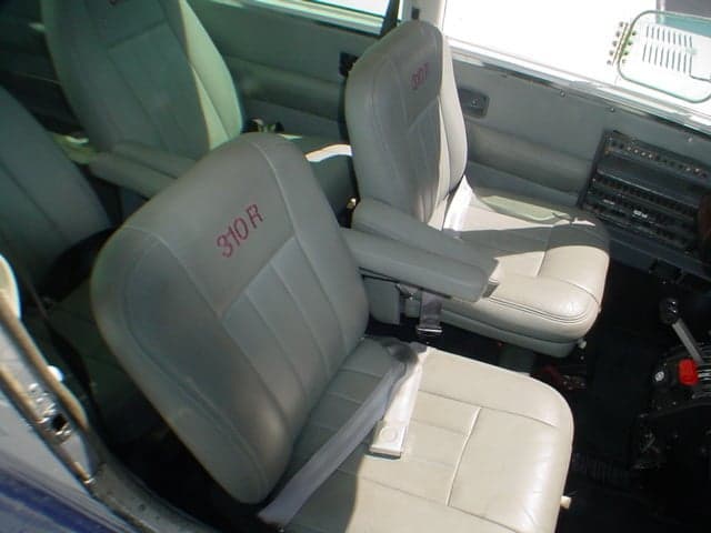 Interior view of the aircraft cabin showing light gray leather seats with "310 R" embroidered on the headrests.