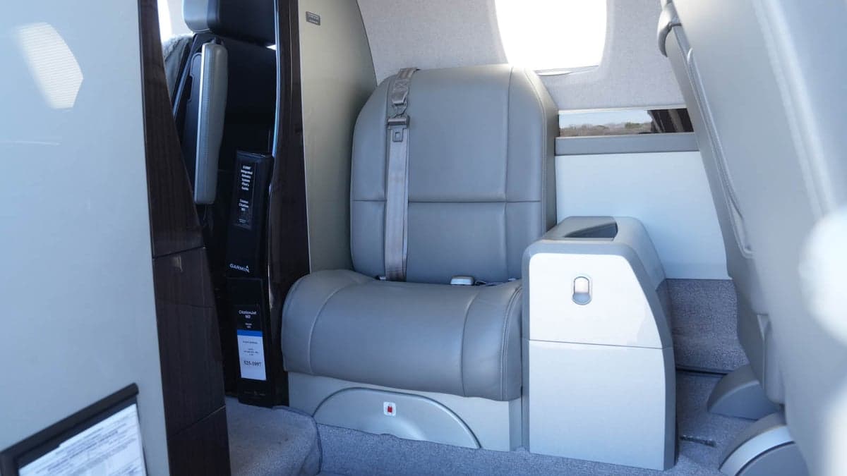 A single gray leather seat is shown inside the aircraft cabin.