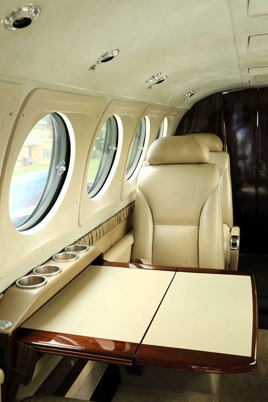 A beige leather seat and a fold-out table with cup holders in the interior cabin of a private jet.