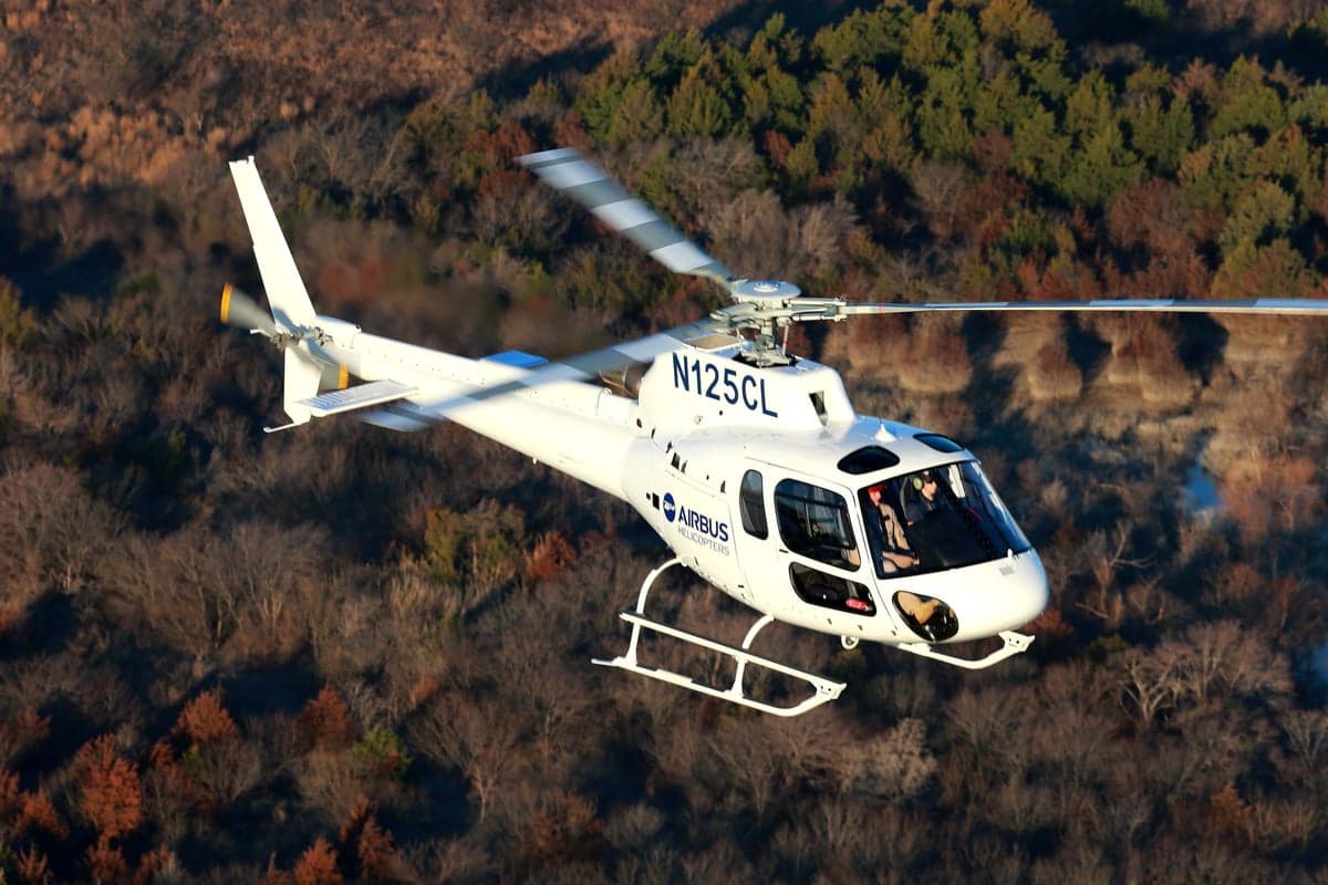 An Airbus Helicopters H125 flying over a forest.