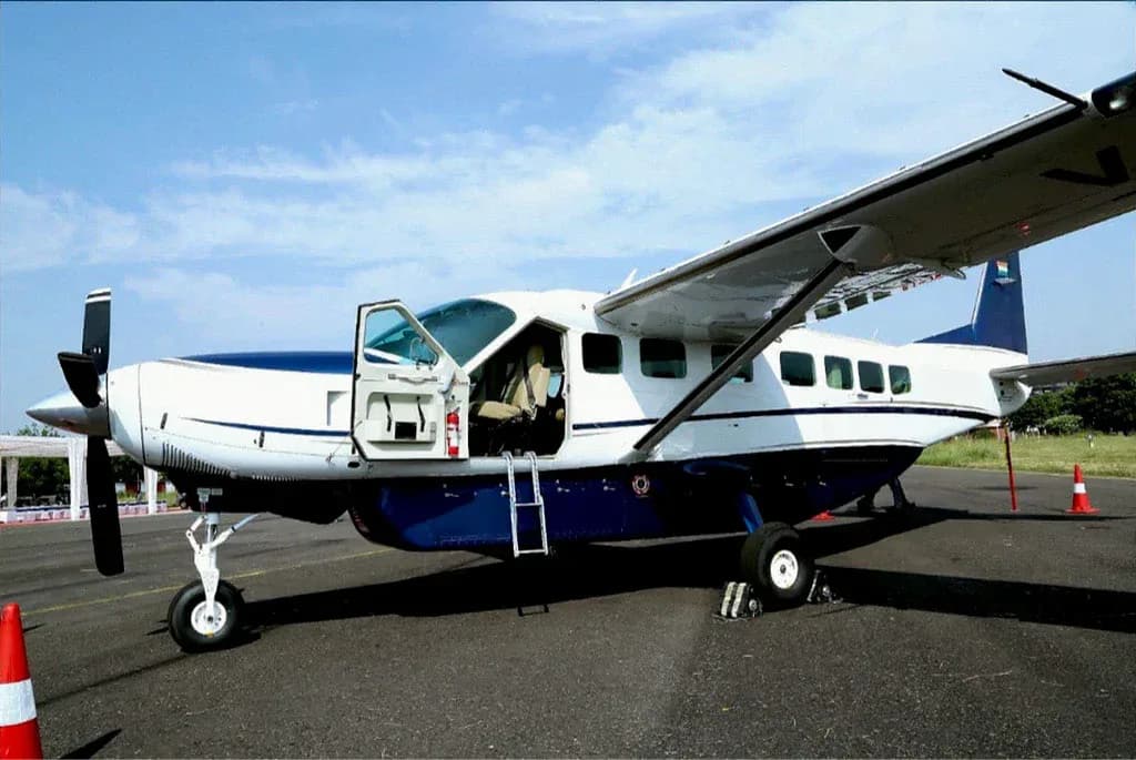 A white and blue single-engine turboprop aircraft with its door open and a ladder extended, parked on an asphalt runway.