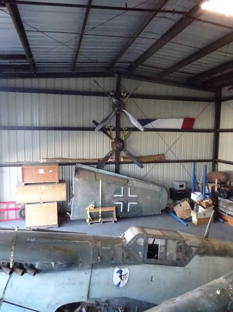 A disassembled Messerschmitt Bf 109 aircraft in a hangar, showing the tail and fuselage.
