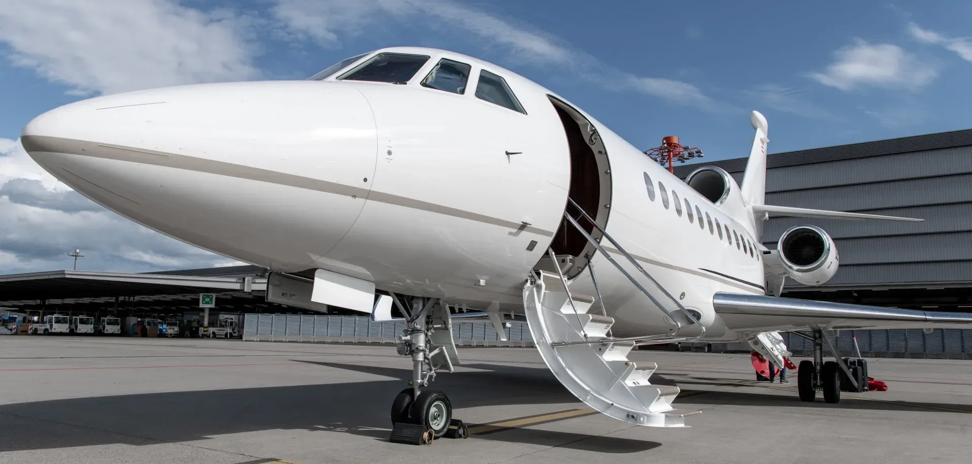 A white business jet with its main door open and stairs extended, parked on an airport tarmac under a blue sky.