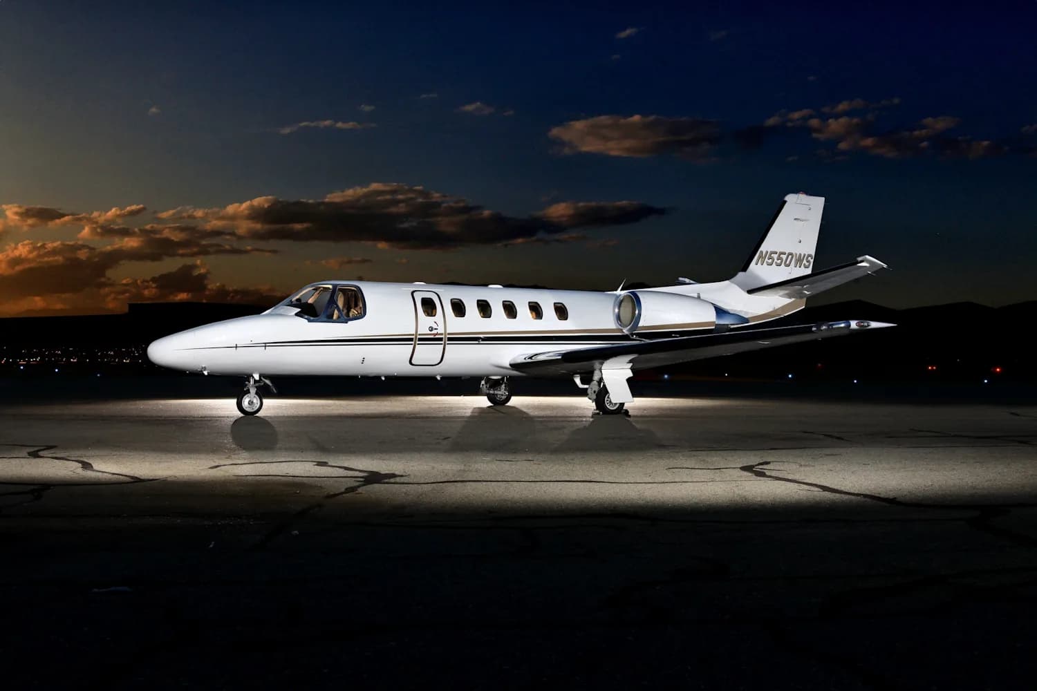 A white jet sits on the tarmac at night with the city lights in the background.