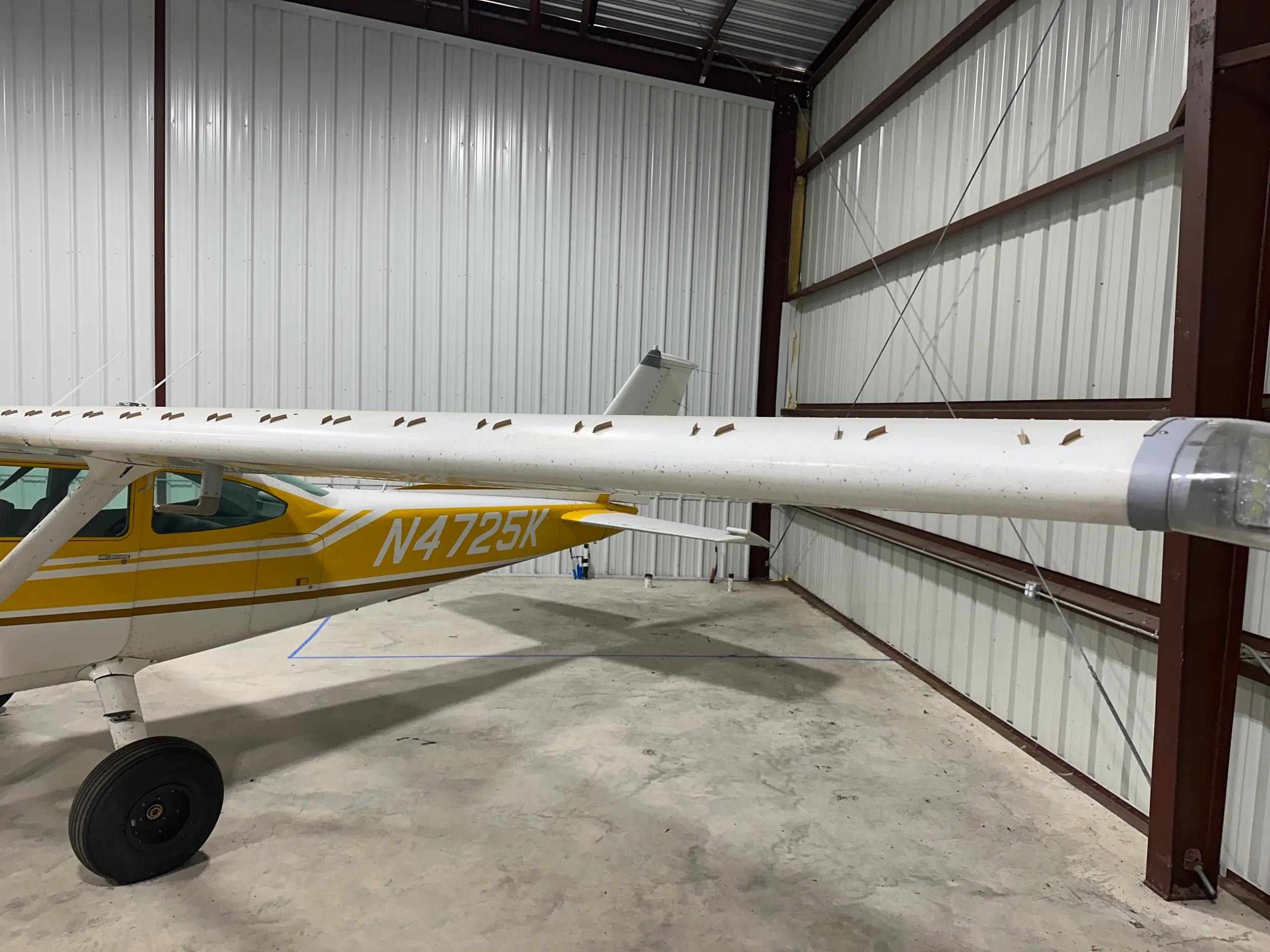 A close-up view of the right wing and rear fuselage of the yellow and white Cessna 172, N4725K, in a hangar.