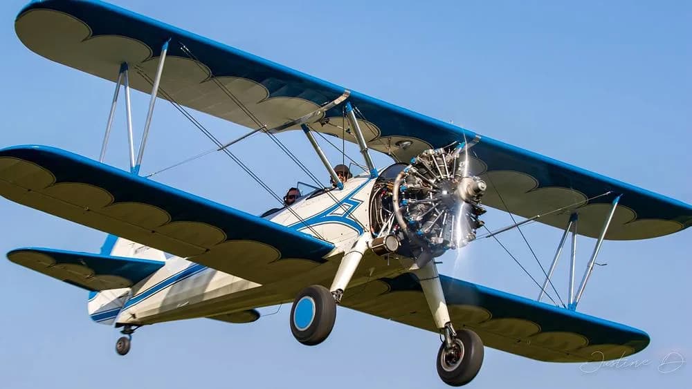 A white and blue biplane with a radial engine in flight against a clear blue sky.