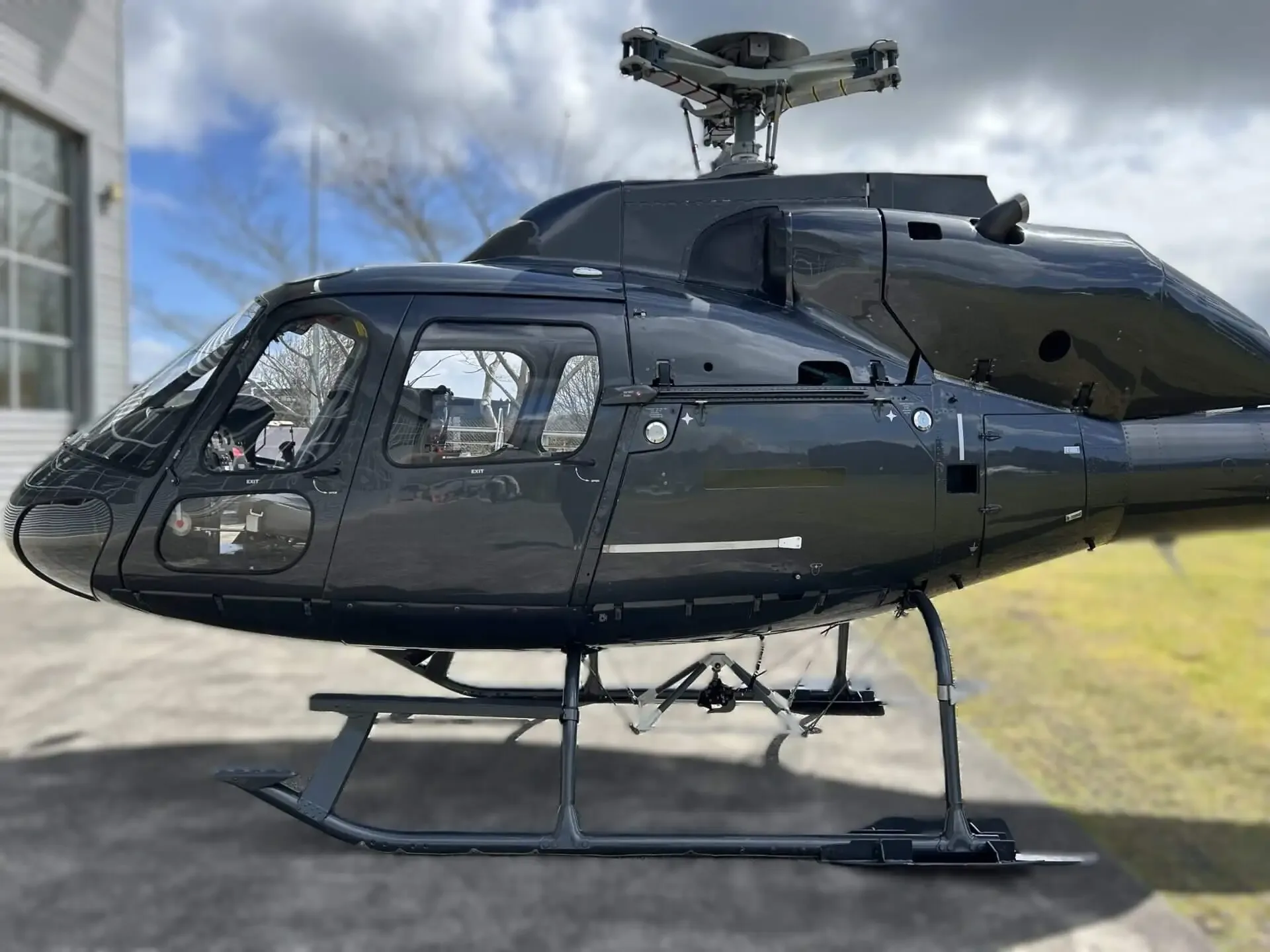 A clear side profile of a dark grey Eurocopter AS355 F1 helicopter, showing its main cabin and landing skids.
