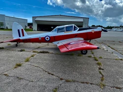 Side view of a red and white aircraft with British markings parked in front of a hangar.