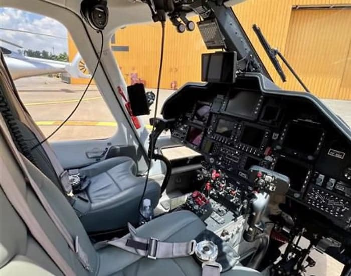The cockpit of a helicopter with gray leather seats and a complex instrument panel.
