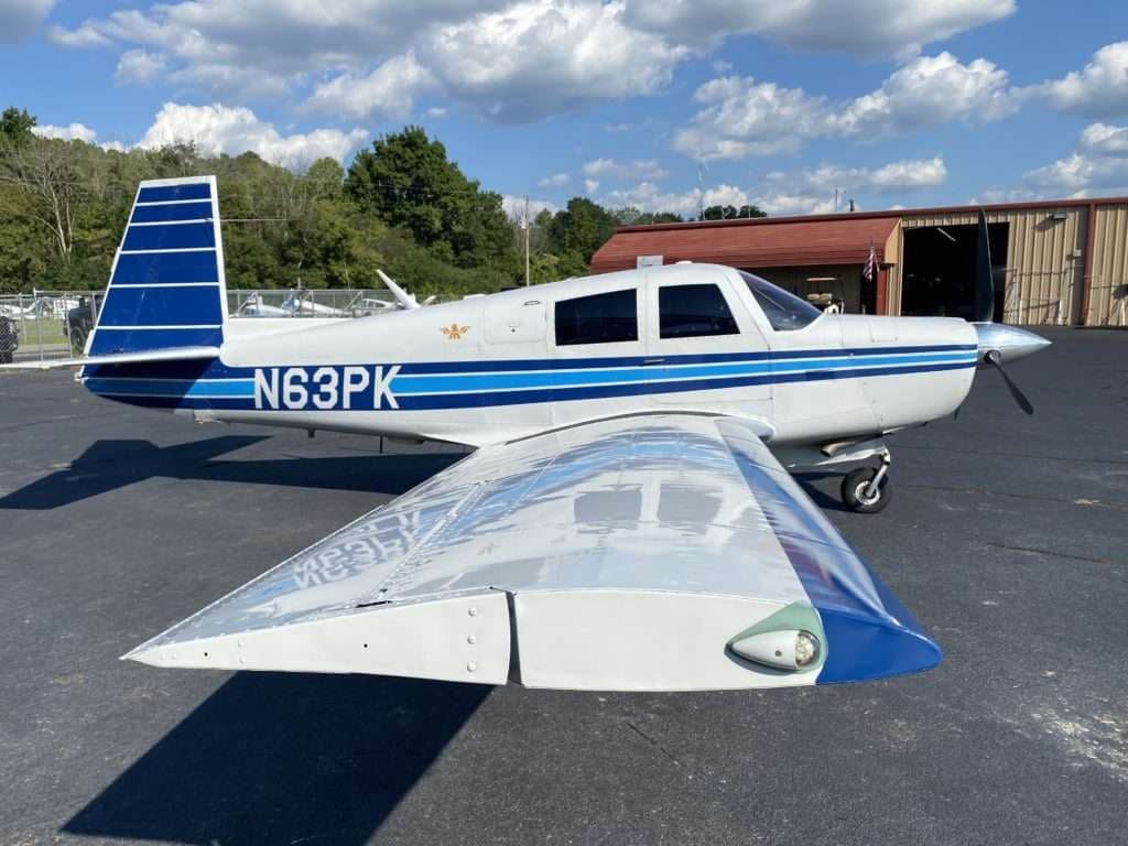 A white and blue Mooney M20C aircraft, tail number N63PK, parked on the tarmac.