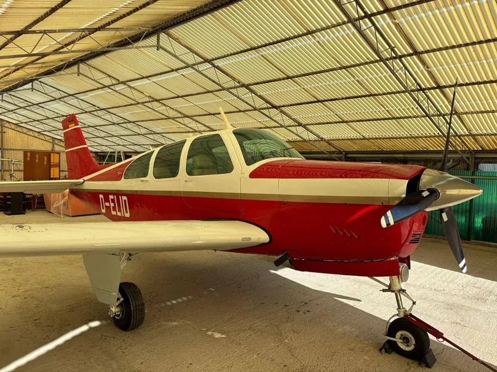 A red and white Beechcraft Bonanza aircraft with registration D-ELID parked inside a hangar.