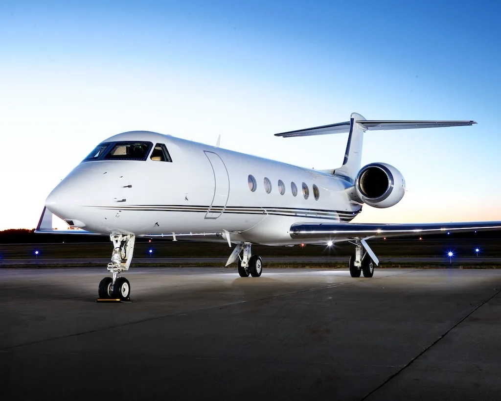 A white Gulfstream G650 business jet with registration F-GBSC parked on a tarmac at sunrise or sunset.