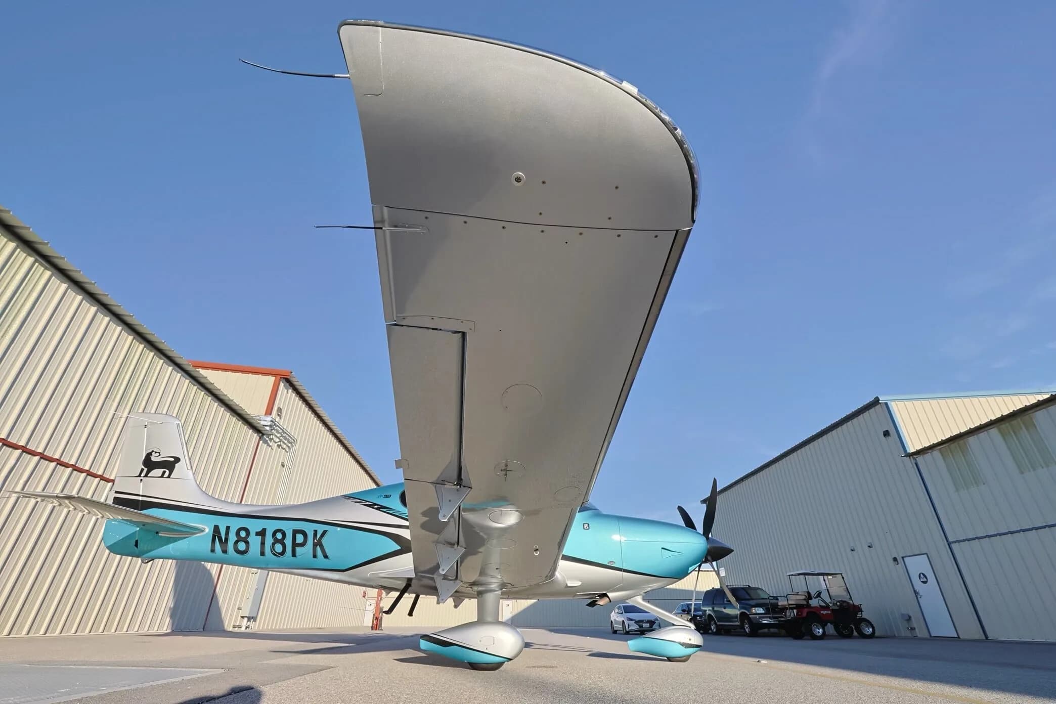 An upward view of the right wing and fuselage of a teal and silver Cirrus SR22T GTS aircraft (N818PK).