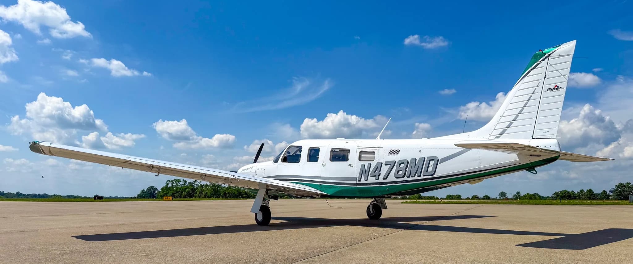 A side view of the white and green Piper Saratoga II TC aircraft (N478MD) showing the Piper logo on the tail.