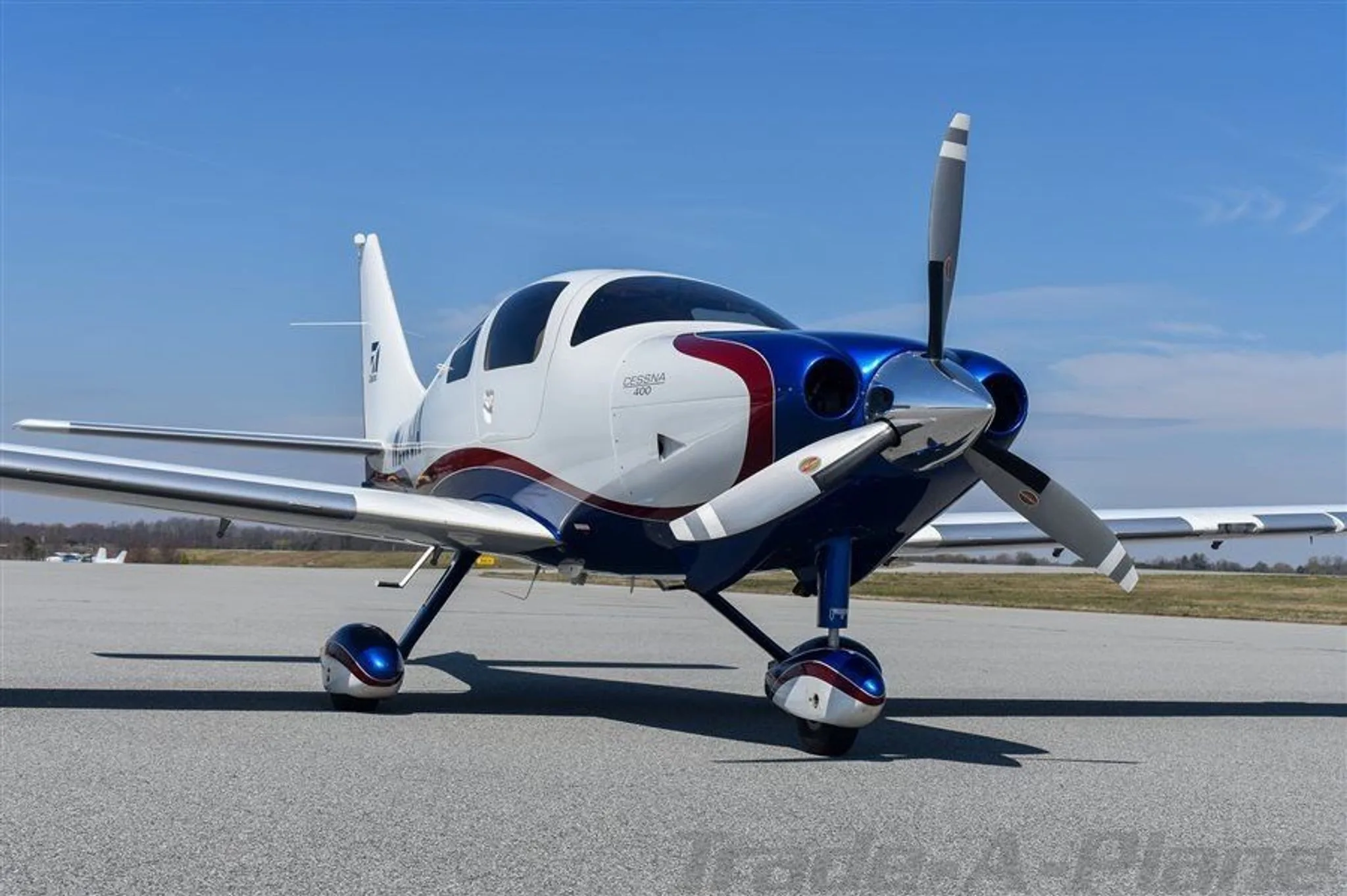 A front-quarter view of the white, blue, and red Cessna 400 aircraft N235JA parked on an airfield.