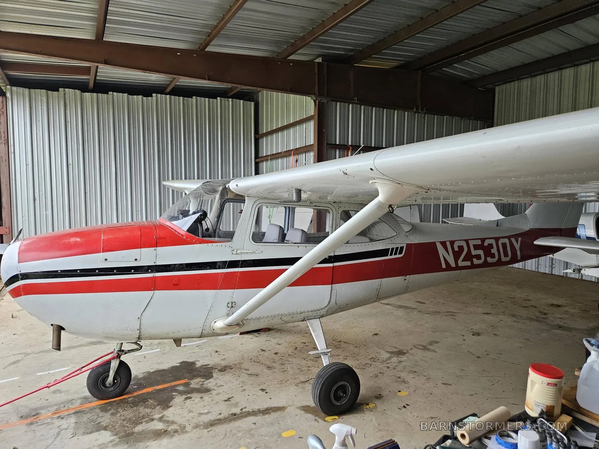 A side view of a white and red single-engine propeller aircraft, N2530Y, parked inside a metal hangar.