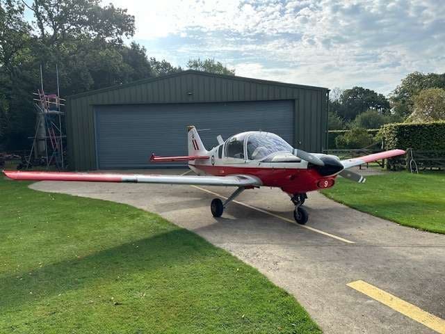 A red and white Bulldog aircraft parked on a paved area in front of a hangar.